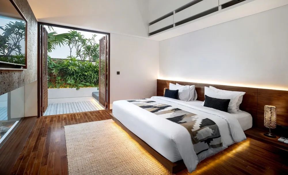 Schlafzimmer mit Doppelbett, Teppich und Zugang zu einer bepflanzten Terrasse.