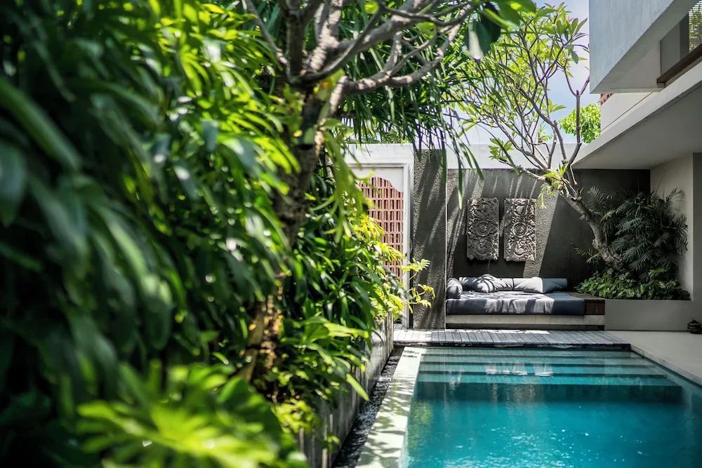 Privater Swimmingpool umgeben von tropischen Pflanzen und einer Liegeecke im Garten.