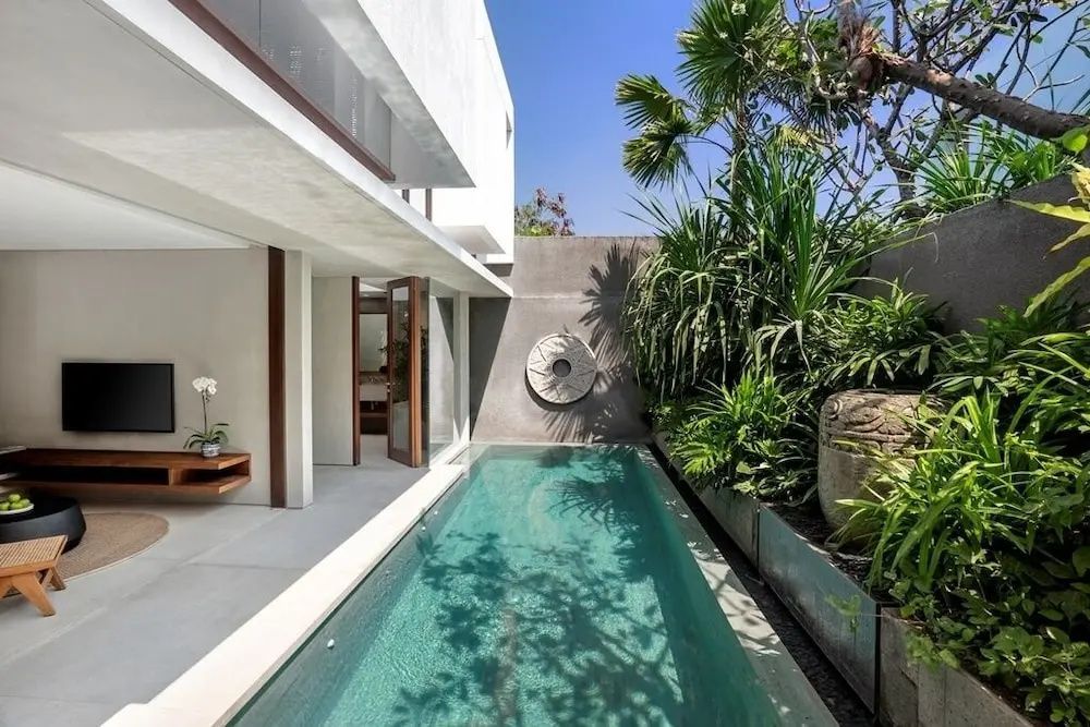 Schmaler Pool im Innenhof einer modernen Villa mit tropischer Bepflanzung.