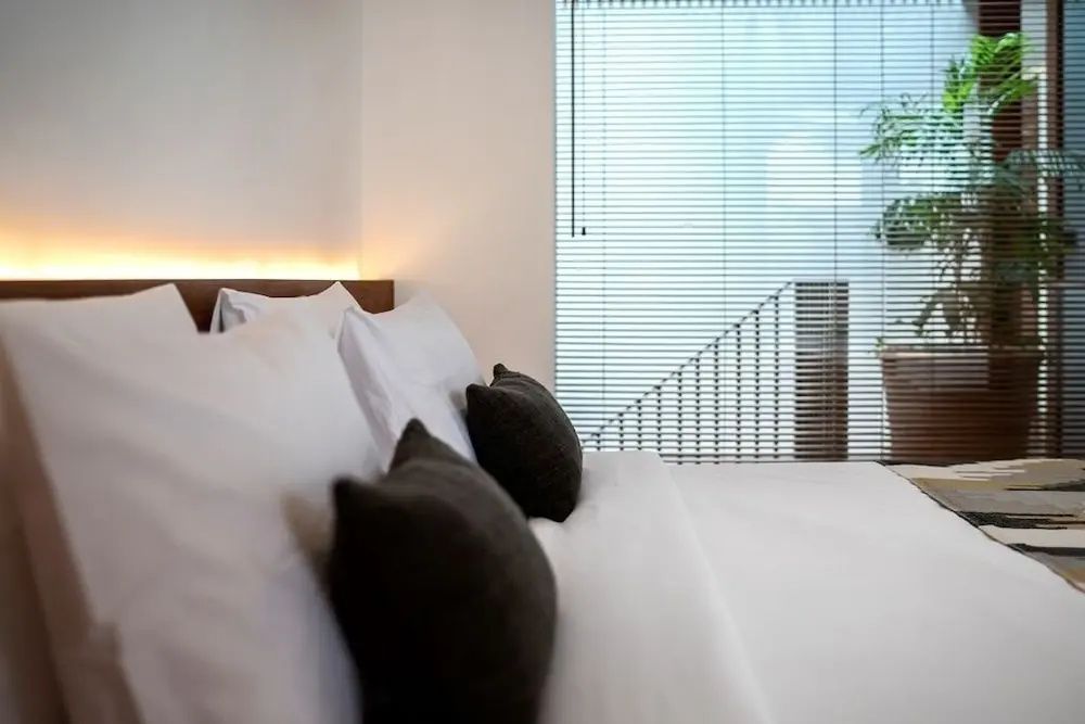 Doppelbett mit weißen und dunklen Kissen sowie dezent beleuchtetem Kopfteil.