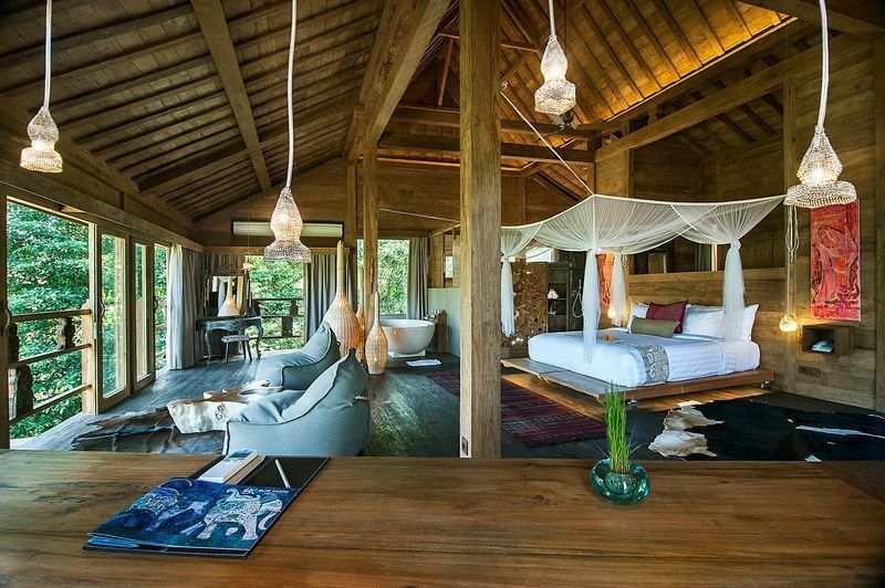 Offenes Schlafzimmer aus Holz mit großem Bett, Moskitonetz und freistehender Badewanne.