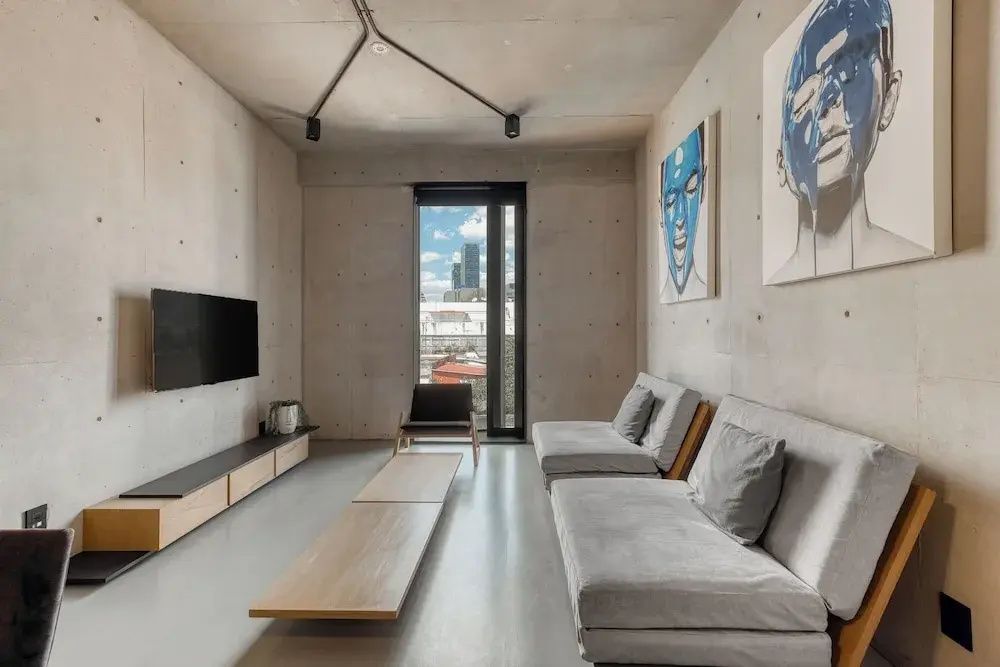 Modernes Wohnzimmer mit grauen Sofas, flachem Holztisch, Sichtbetonwand und großem Fenster.