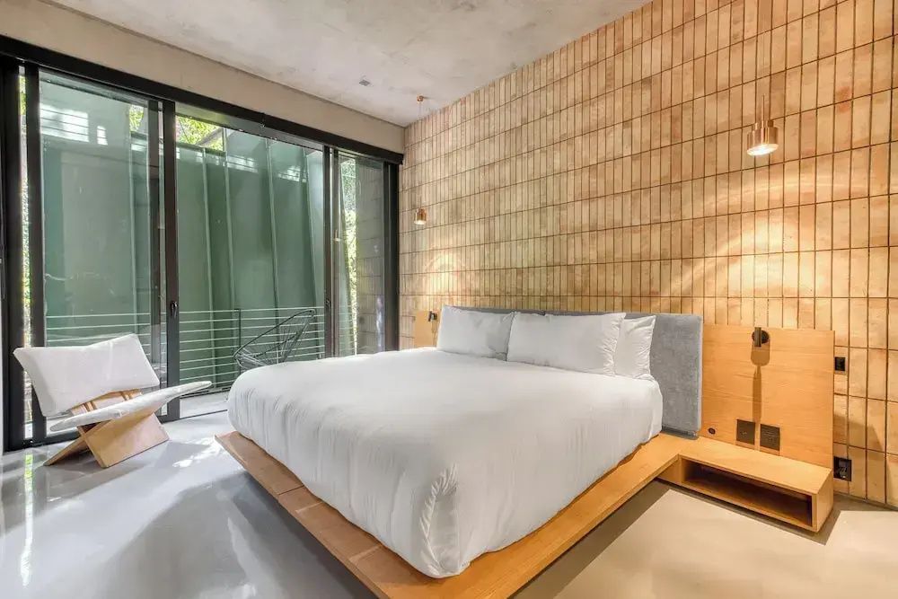 Hell eingerichtetes Schlafzimmer mit großem Doppelbett und Fliesendekorwand.