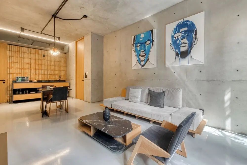 Moderne Wohnzimmereinrichtung mit hellem Sofa, Sessel, Couchtisch und Kunstwerken an einer Sichtbetonwand.