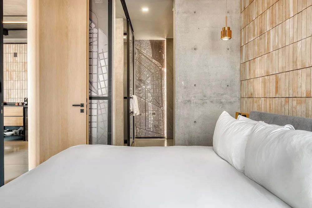 Schlafbereich mit weißem Bett, gläserner Schiebetür und einer rustikalen Betonwand.