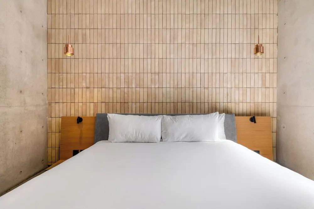 Doppelbett mit zwei Kissen vor einer Wand aus beigen vertikalen Fliesen.