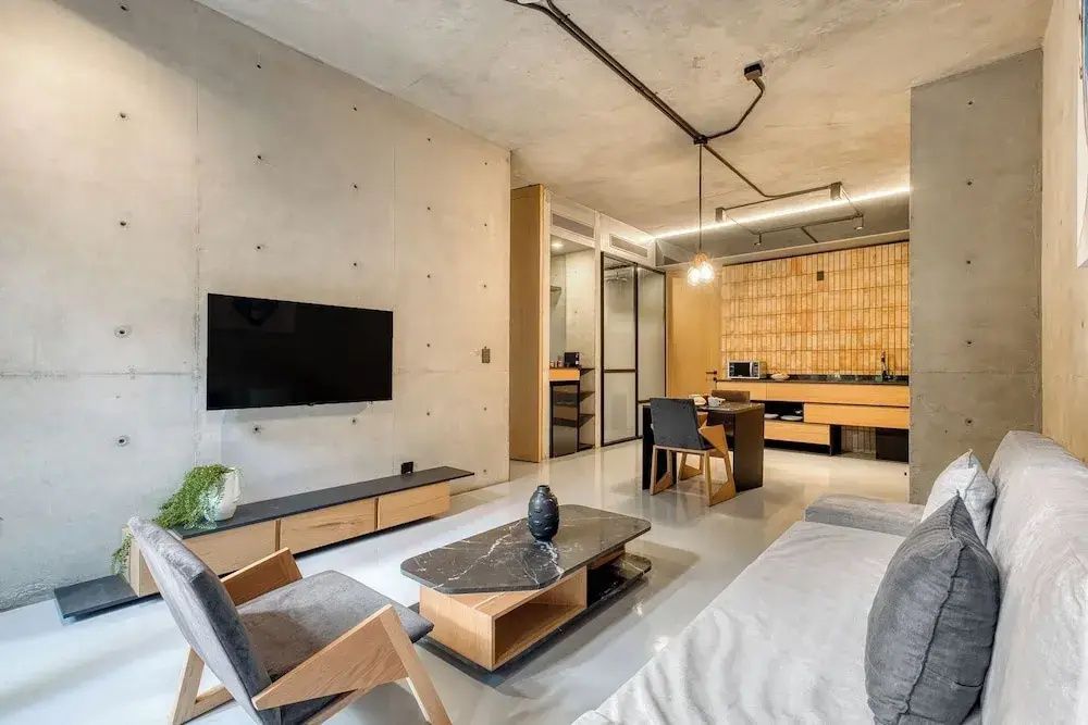 Geräumiger Wohnbereich mit Wand-Fernseher, Couchtisch, Sessel, Essplatz und offener Küchenzeile.