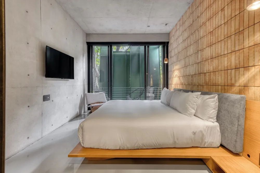 Schlafzimmer mit Doppelbett, Flachbildfernseher an der Sichtbetonwand und Fenster.