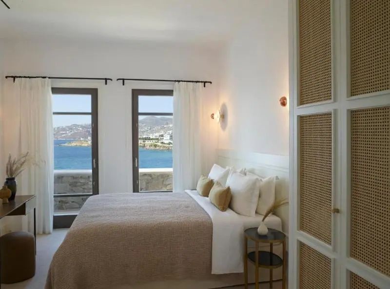 Hell eingerichtetes Schlafzimmer mit Doppelbett, Nachttisch und Meerblick.