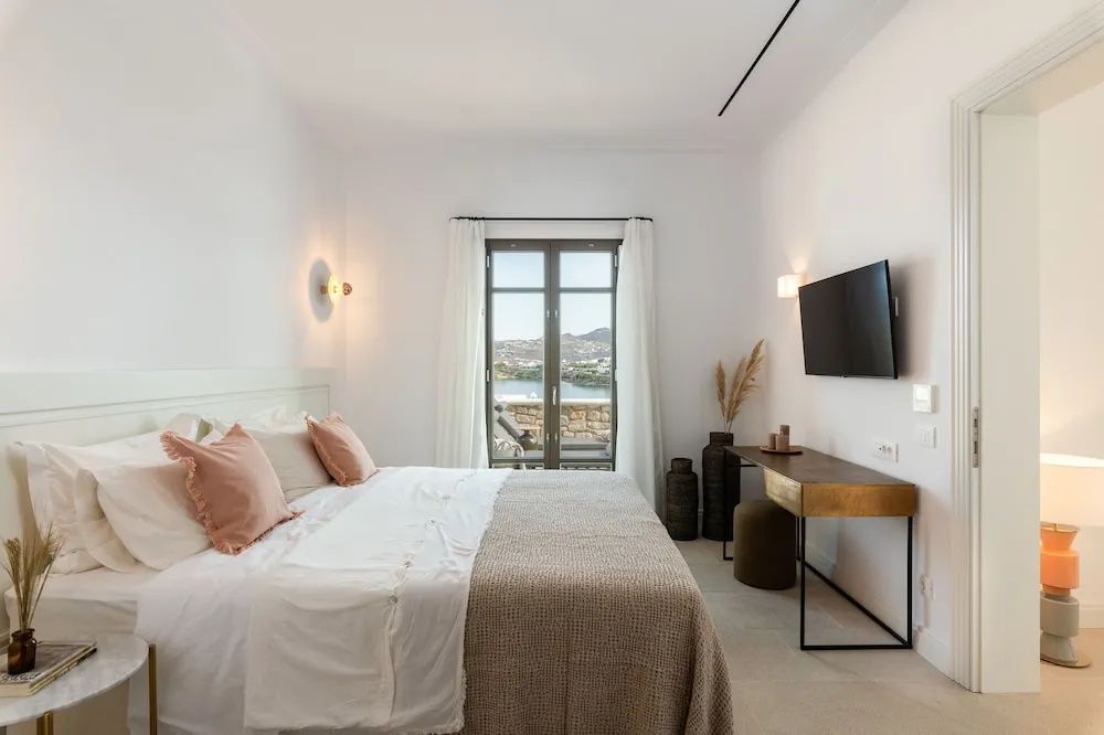 Hell eingerichtetes Schlafzimmer mit Doppelbett, Wandfernseher und Schreibtisch.