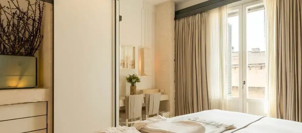 Heller Schreibtischbereich im Hotelzimmer mit zwei Stühlen, Wandlampe und Vorhängen.