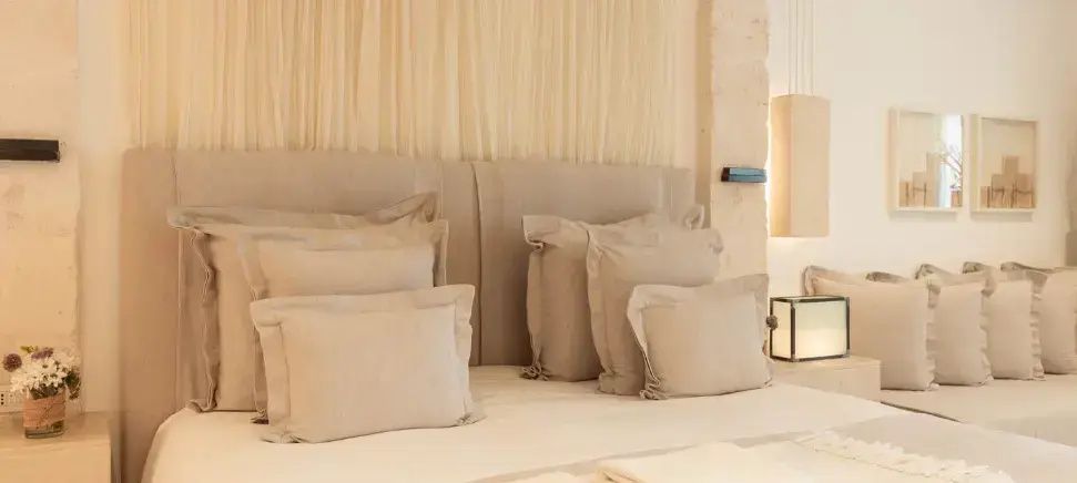 Bett mit mehreren cremefarbenen Kissen und stoffbespanntem Kopfteil im Zimmer.