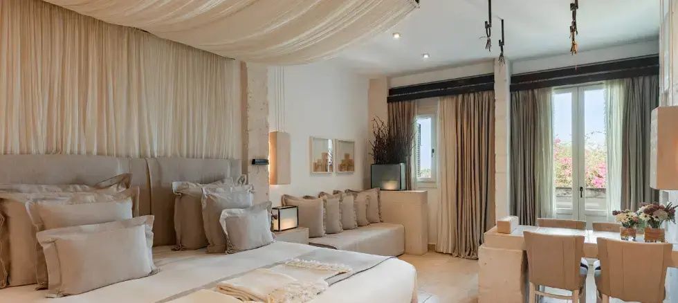 Helles Hotelzimmer mit großem Doppelbett, Baldachin und beigefarbenem Sofa.
