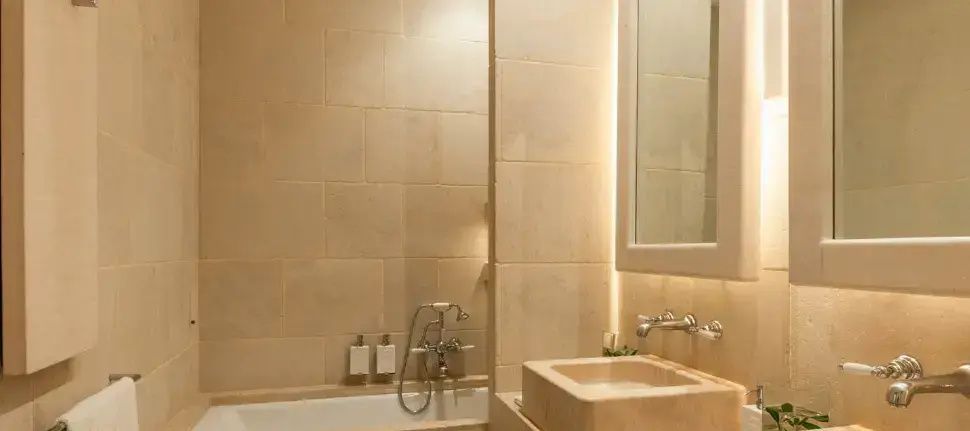 Badezimmer mit einem Waschtisch aus Naturstein und hellem Fliesenbelag.