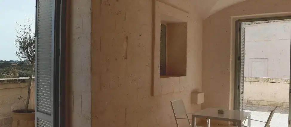 Helle Natursteinwand auf einer Terrasse mit rechteckigem Nischenfenster und Sitzgelegenheit.