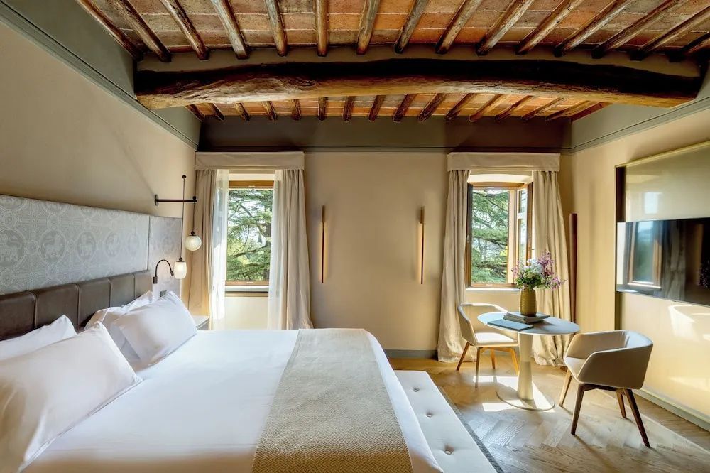 Hotelzimmer mit Holzbalkendecke, Doppelbett, Sitzbereich mit Tisch und zwei Fenstern ins Grüne.