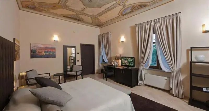 Hoher Raum mit bemaltem Deckenfresko, Doppelbett, Fernseher und Vorhängen.