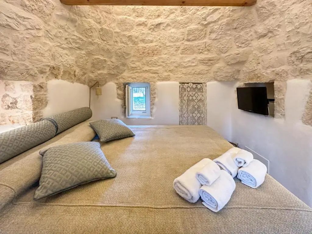 Schlafbereich mit Natursteinwänden, einem Doppelbett, Handtüchern und kleinem Fenster.