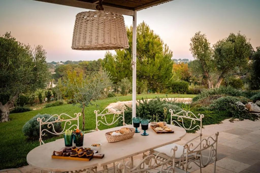 Gedeckter Tisch auf einer überdachten Terrasse mit Blick ins Grüne und verzierten Metallstühlen.