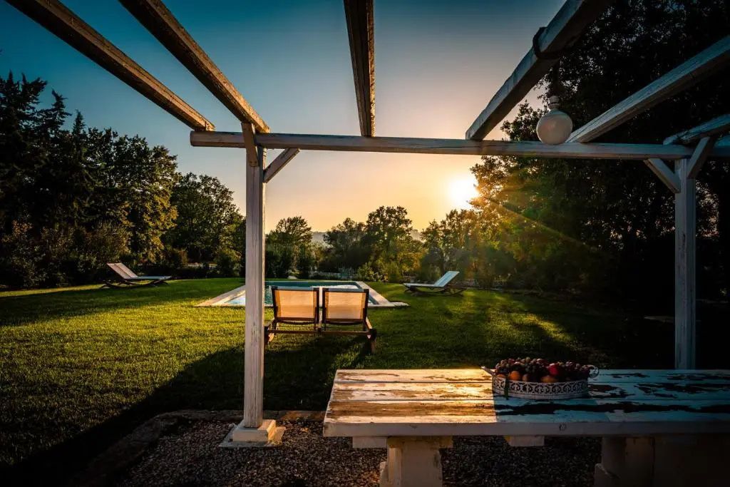 Blick von einer Holzpergola über den Garten und den Pool bei Abendlicht