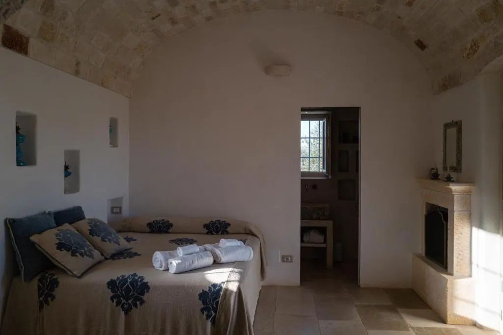 Schlafzimmer mit Steingewölbe, einem Doppelbett mit gemusterter Tagesdecke und Blick ins Bad.