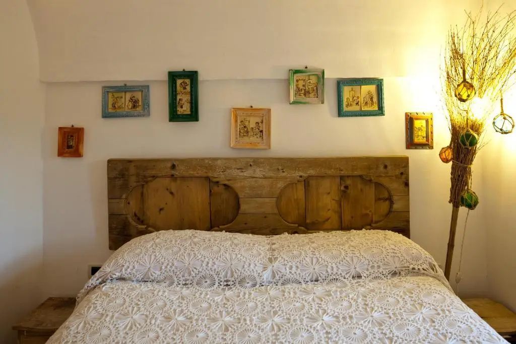 Doppelbett mit gehäkelter Tagesdecke, rustikalem Kopfteil aus Holz und kleinen Bildern an der Wand.