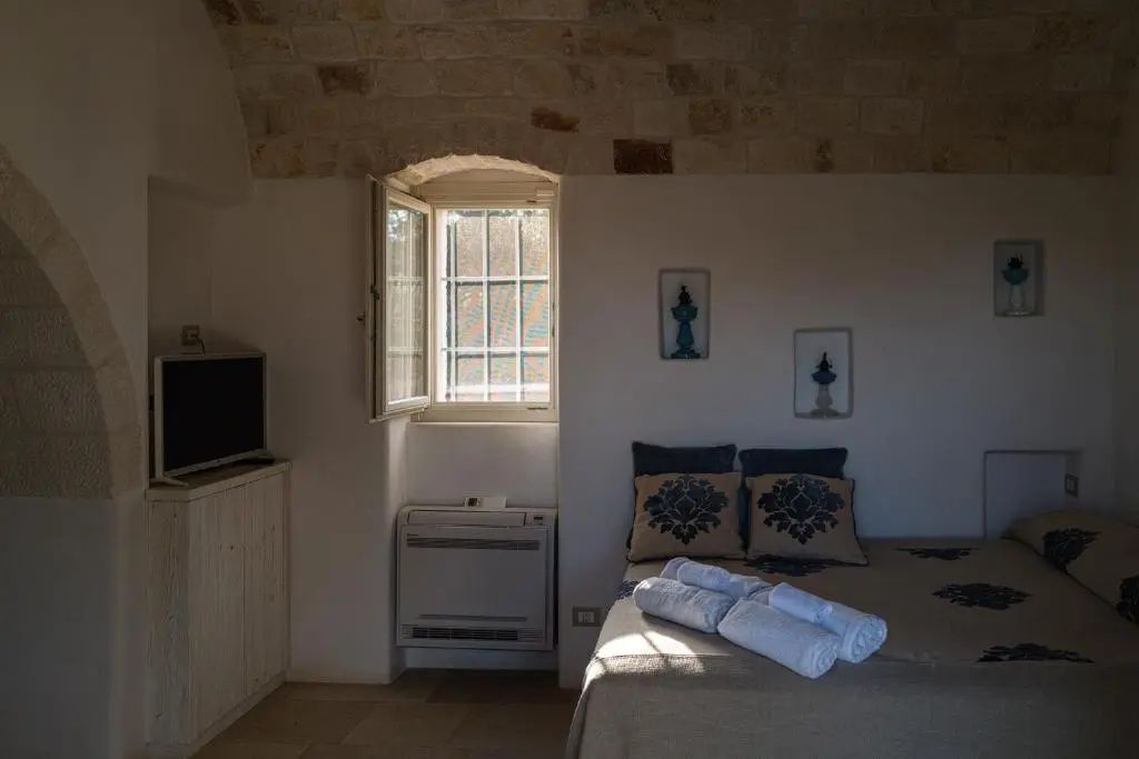Helles Schlafzimmer mit offenem Fenster, Doppelbett und einem Natursteingewölbe.
