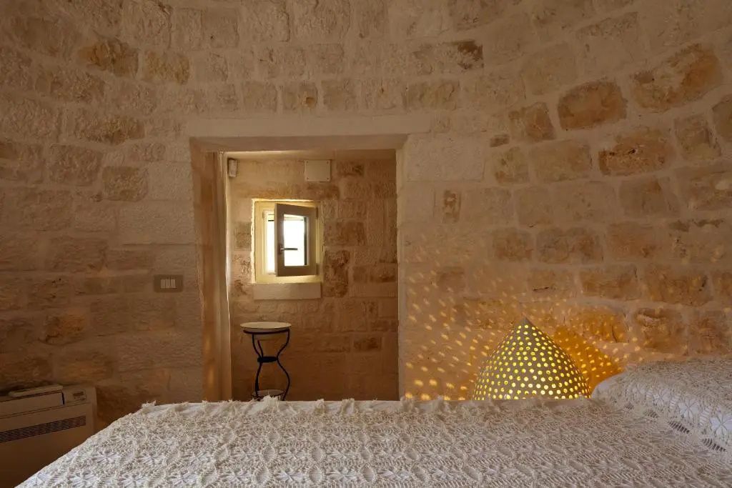 Schlafzimmer in einem Natursteingewölbe mit einem Doppelbett und beleuchtetem Lampenschirm.