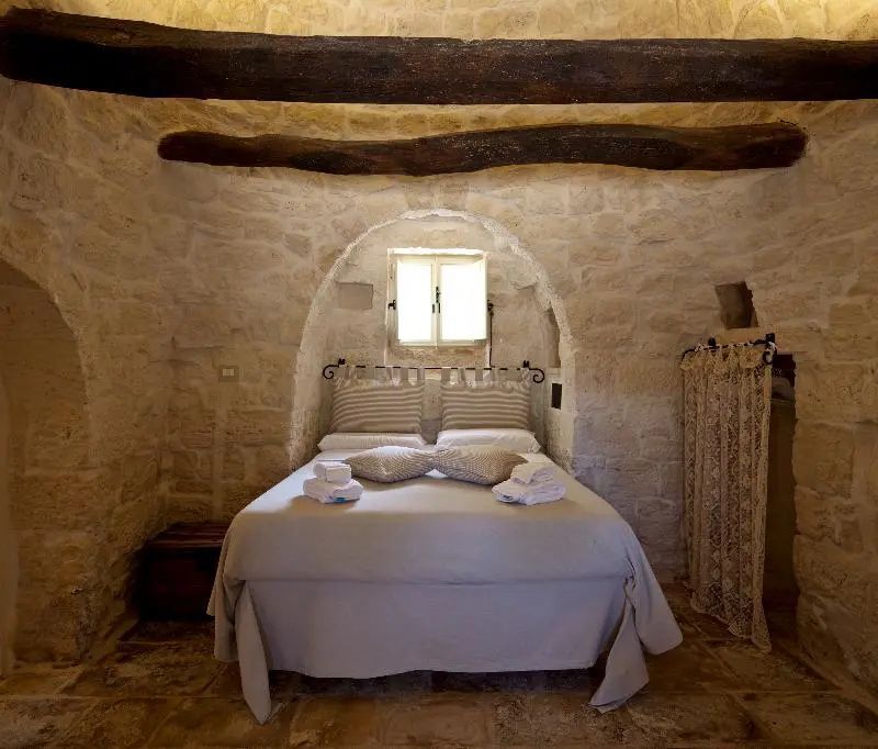 Schlafbereich in einem Natursteinraum mit Holzbalkendecke und einem Doppelbett unter einer Steinarchitektur.