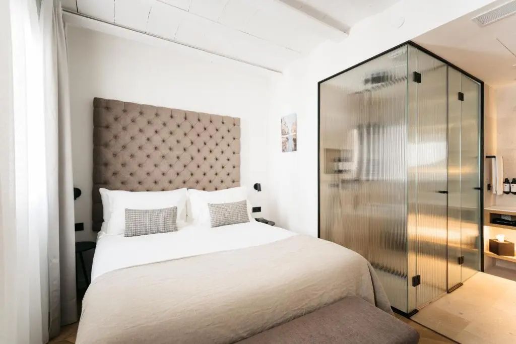 Hotelzimmer mit braunem Kopfteil am Doppelbett und gläserner Duschkabine.