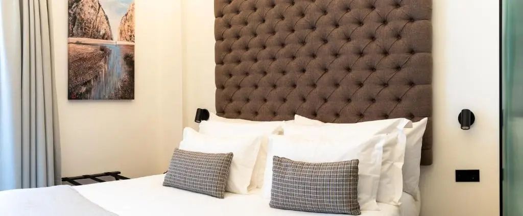 Detailansicht eines gepolsterten Kopfteils mit Kissen auf dem weiß bezogenen Bett.