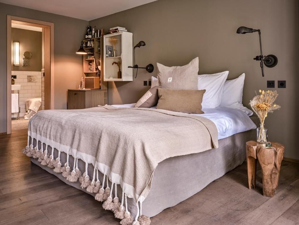 Doppelbett mit beigen Kissen und Decke mit Quasten in einem hellen Hotelzimmer.