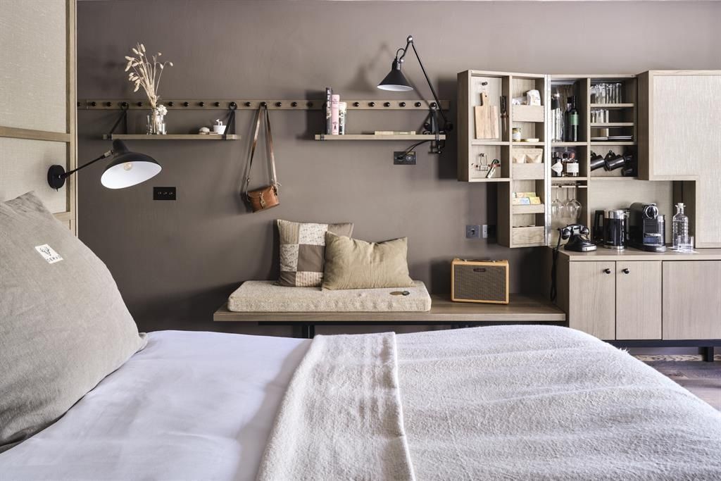 Holzregal an der Wand mit Gläsern und Minibar sowie einer kleinen Sitzbank im Zimmer.