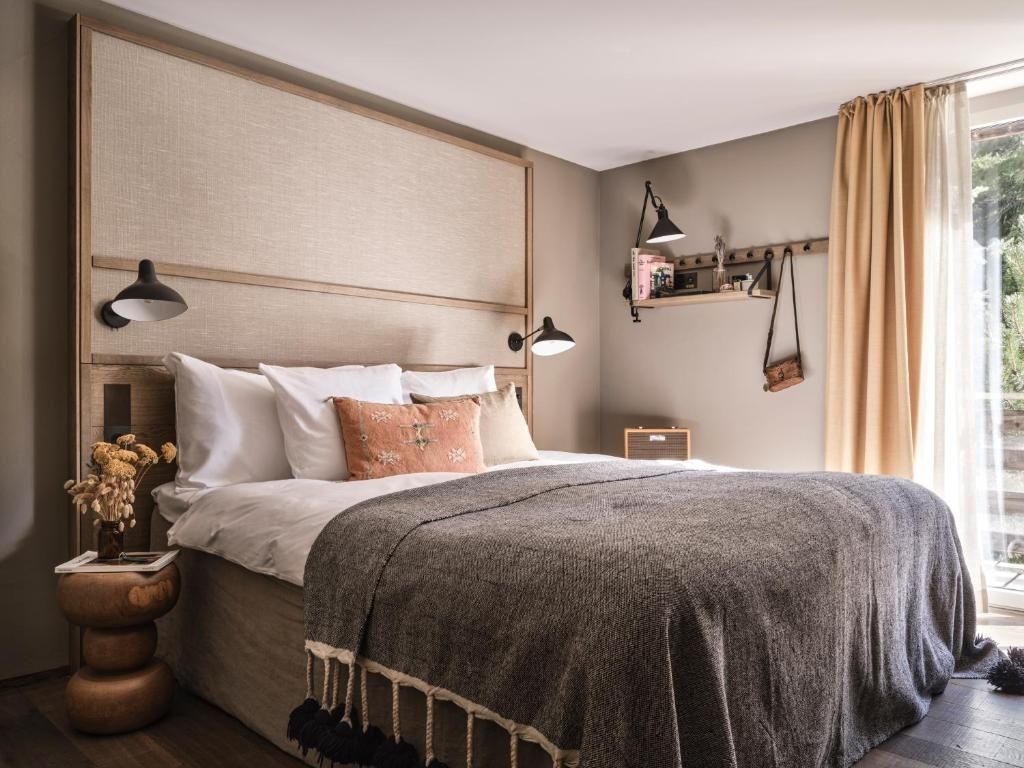 Doppelbett mit beigefarbenem Kopfteil, Wandlampe und Decke mit Quasten.