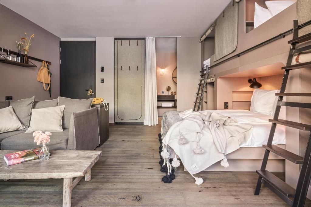 Modernes Hotelzimmer mit grauem Sofa, Holztisch und Schlafmöglichkeiten aus Holz.