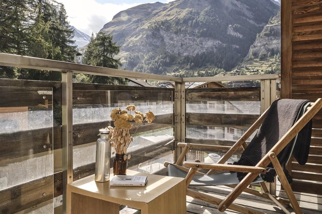 Balkon mit Holzstuhl, kleinem Tisch und Blick auf eine Berglandschaft.