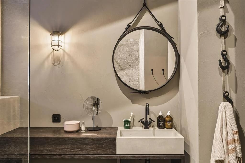 Waschtisch mit eckigem Waschbecken, rundem Hängespiegel und Seifenspendern.