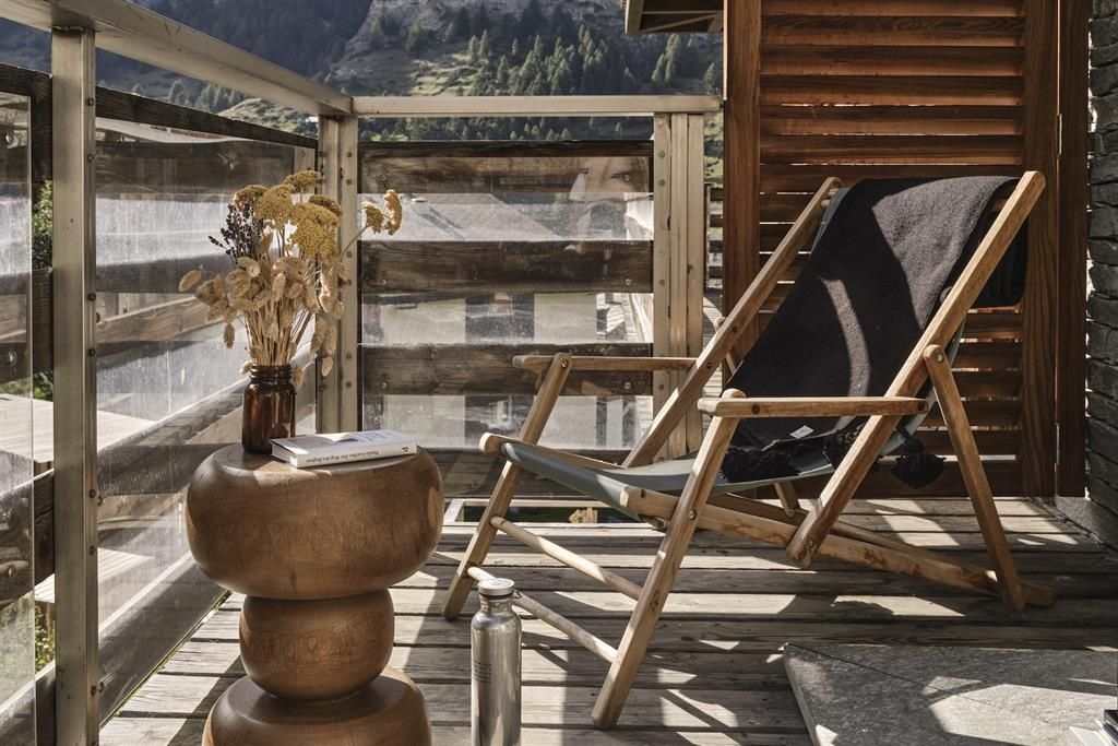 Sitzbereich auf dem Balkon mit Liegestuhl aus Holz und Beistelltisch vor Bergkulisse.