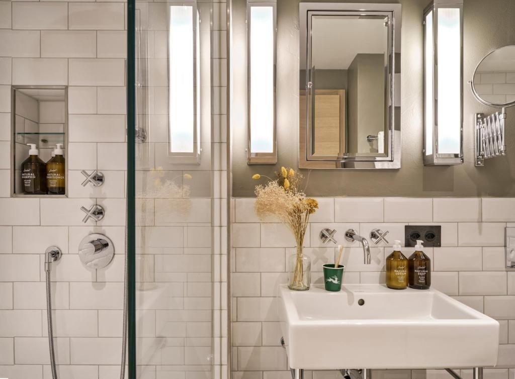 Badezimmer mit weißem Waschbecken, rechteckigem Spiegel und Dusche hinter Glas.