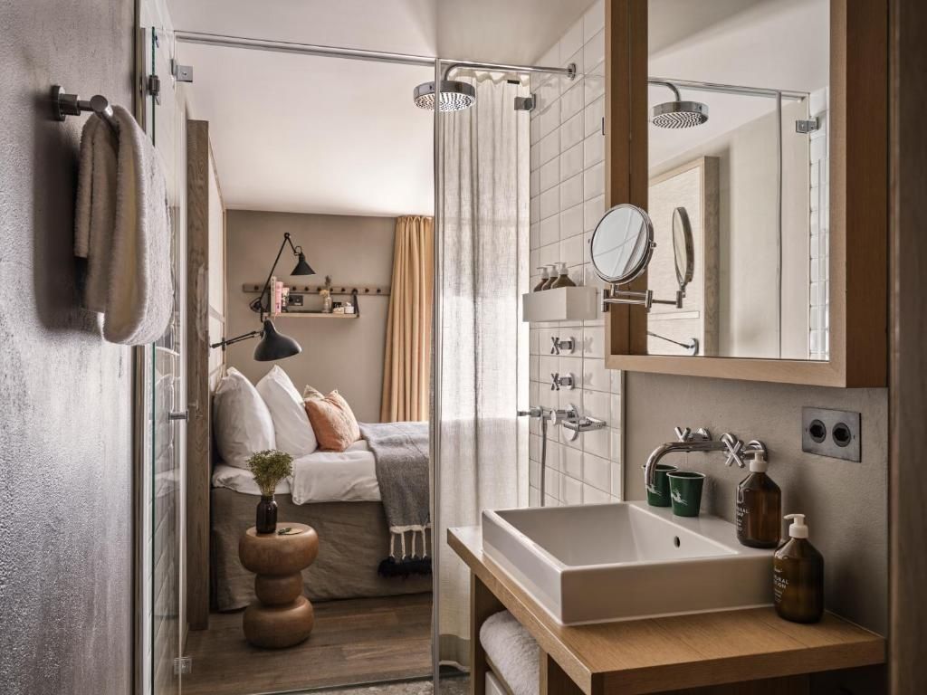 Badezimmer mit Waschtisch aus Holz, weißem Waschbecken und Blick auf das Bett.