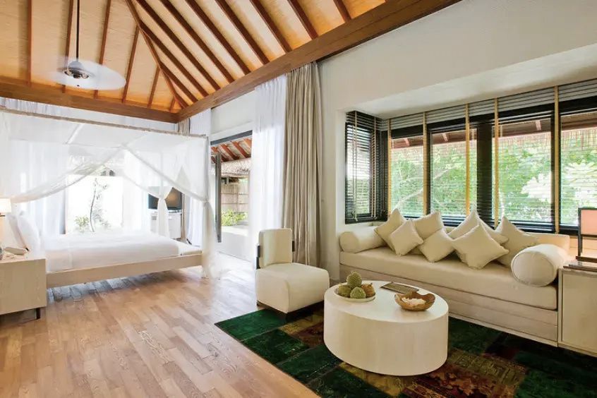 Heller Wohnraum einer Villa mit beigefarbenem Sofa, Holzfußboden und Blick zum Himmelbett.
