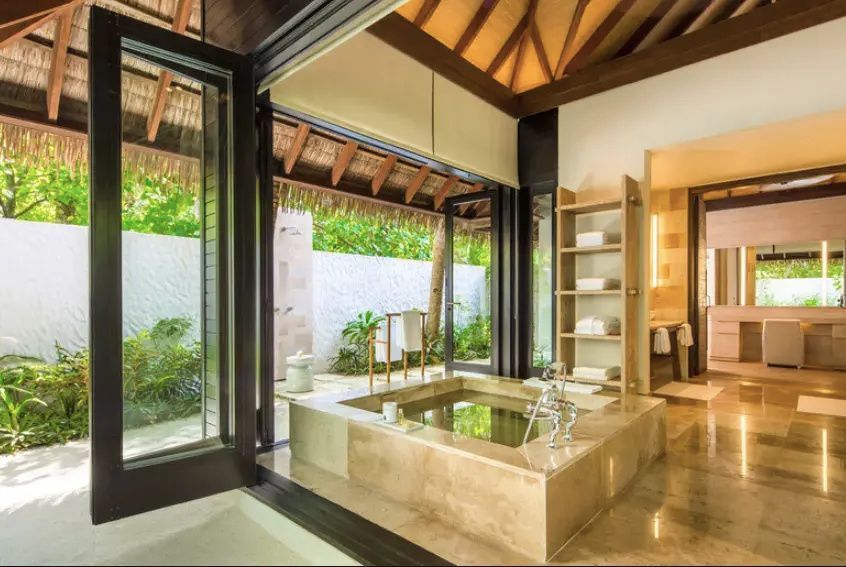Badezimmer einer Villa mit versenkter Badewanne aus Stein und offenem Zugang zum Garten.