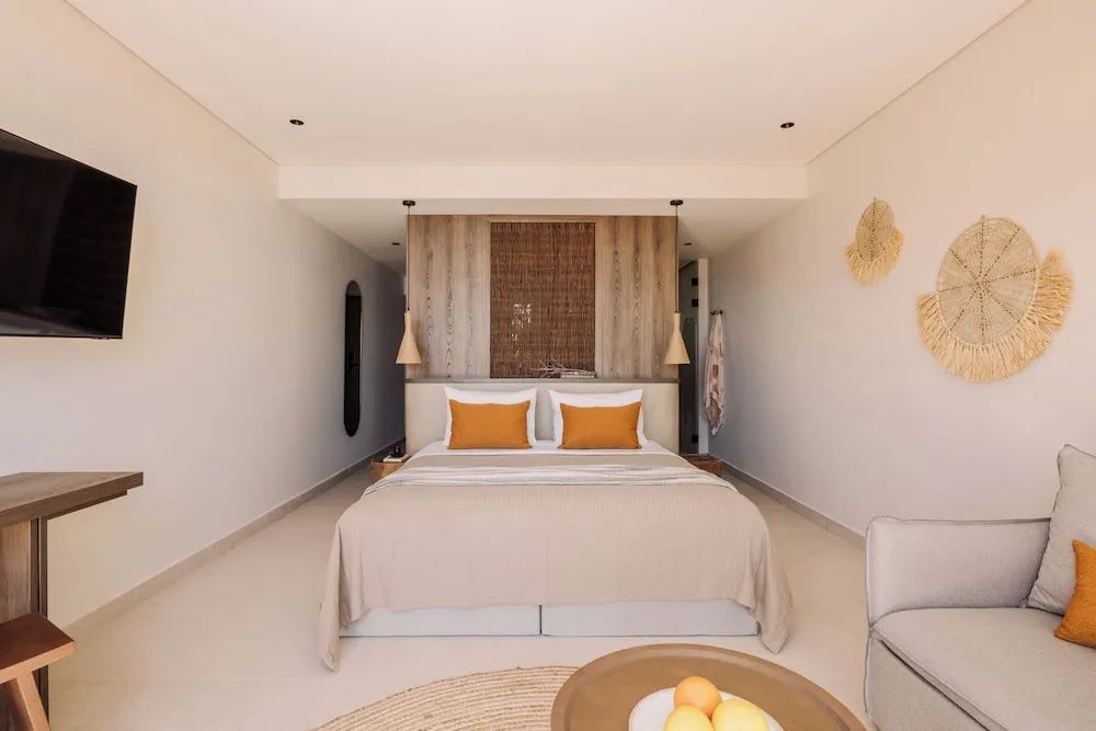 Hell eingerichtetes Schlafzimmer mit Doppelbett, orangefarbenen Kissen und Holzdekor.