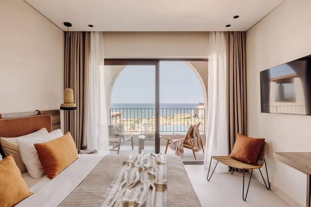 Helles Schlafzimmer mit Doppelbett und Zugang zum Balkon mit Blick aufs Meer.