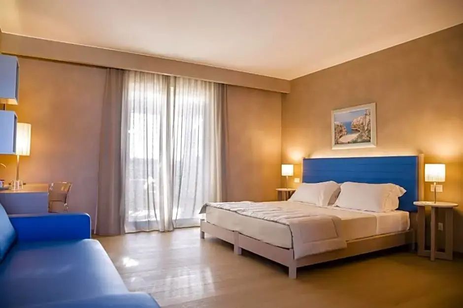 Helles Hotelzimmer mit Doppelbett, blauem Kopfteil und Fenster mit Vorhängen.