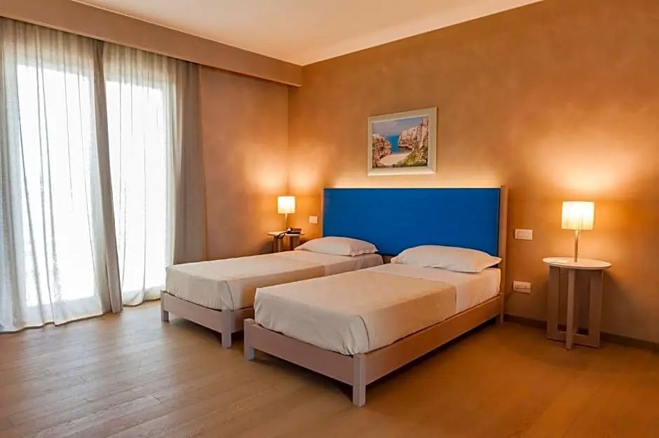 Helles Hotelzimmer mit zwei Einzelbetten, blauem Kopfteil und Nachttisch.