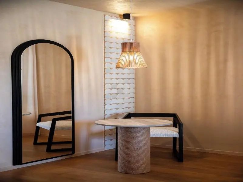 Sitzbereich im Hotelzimmer mit rundem Tisch, Stühlen und einem großen Spiegel.