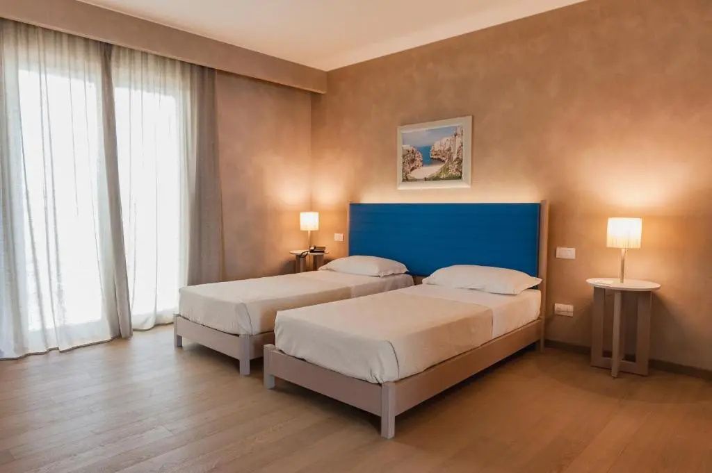 Doppelzimmer mit zwei Einzelbetten, blauem Kopfteil und warmer Wandbeleuchtung.