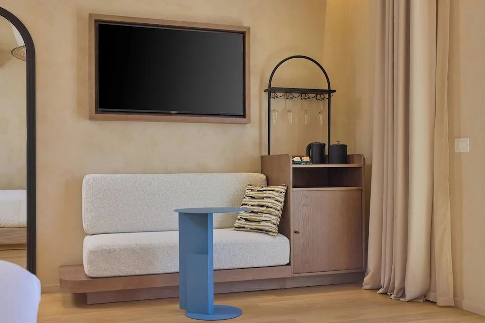 Sitzecke im Hotelzimmer mit hellem Sofa, blauem Beistelltisch und Fernseher an der Wand.