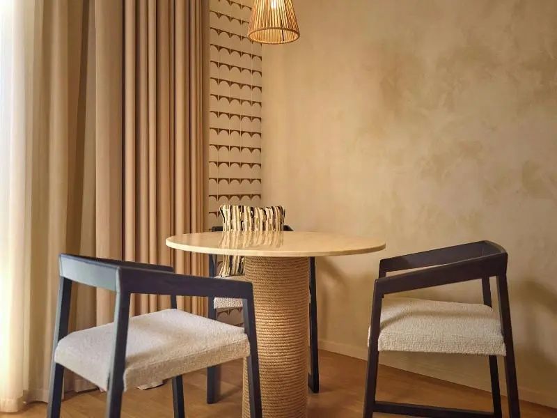 Runder Tisch mit zwei Stühlen vor hellen Vorhängen in einem Hotelzimmer.